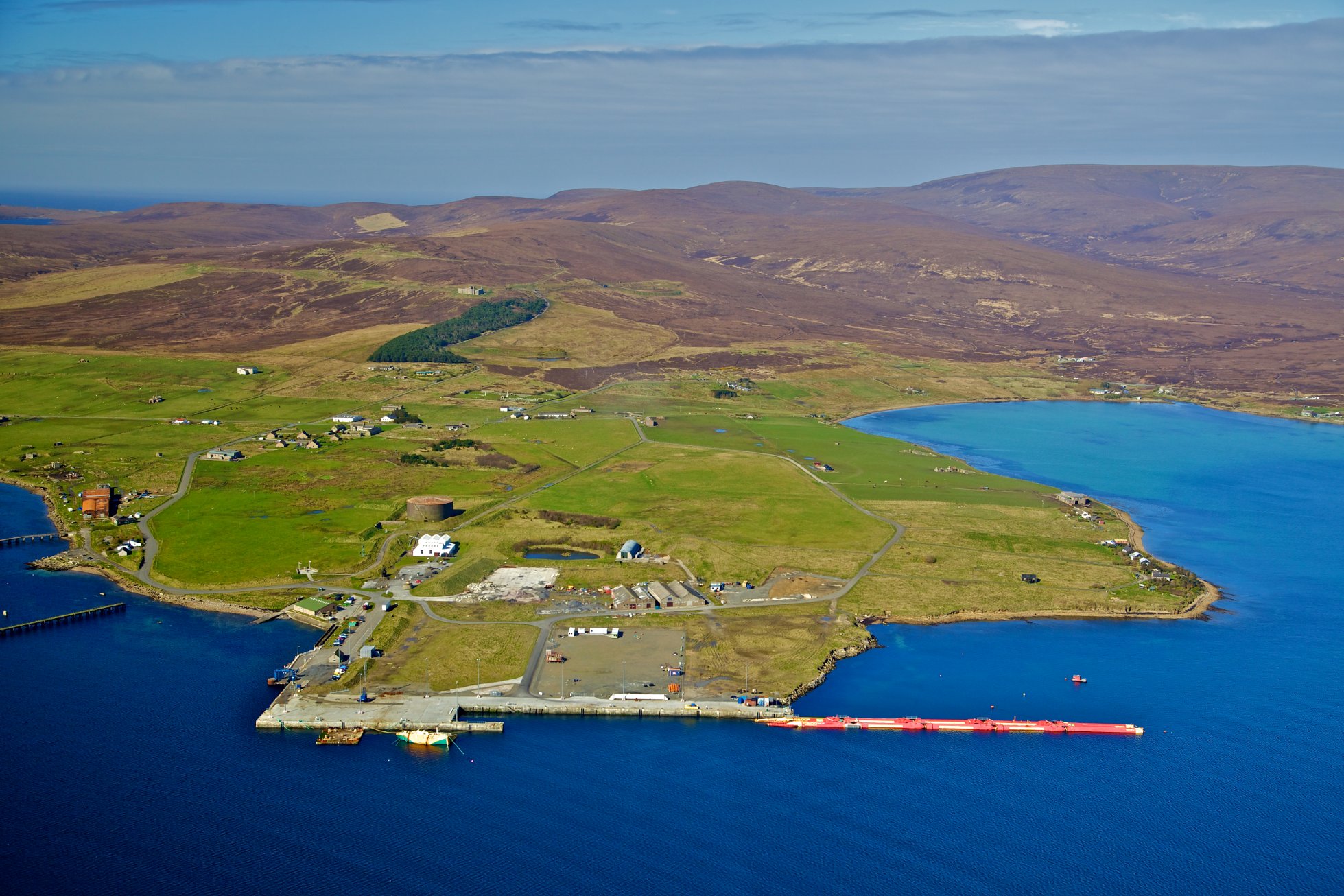 Aerial view of Lyness, Hoy. The oil tanks structure is above and to the right of the patch of woodland. Image by Colin Keldie